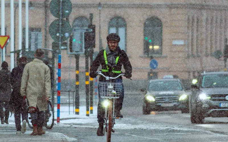 Pendlare med reflexsele och tänt framlyse cyklar i snöslask på stadsgata